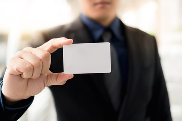 Fototapeta premium Man's hand showing business card : Businessman wearing a black suit showing a white business card in city outdoor. Copy space.
