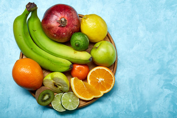 Ripe fresh fruits in a wooden plate on a blue background, selective focus, close-up, top view