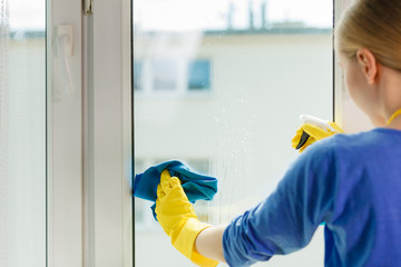Girl cleaning window at home using detergent rag