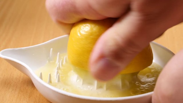 Male hand squeezing fresh lemon fruit using plastic juice squeezer. Making healthy citrus sour drink. Slow motion