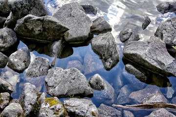 Fototapeta na wymiar Stones and rocks on a transparent surface of lake where reflects mountain Tatras, Poland