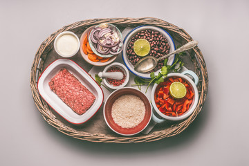 Bowls with ingredients for balanced one pan meal with beans, minced meat, rice and vegetables in tray on gray background, top view