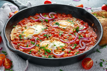 Tasty Breakfast Shakshuka in a Iron Pan. Fried eggs with tomatoes, red, yellow peppers, onion, parsley, Pita bread and herbs. Healthy Food