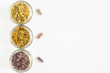 Curative herbs in glass jars and capsules on a white background