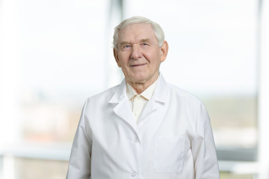 Very old man in white uniform. Gaze of senior physician, portrait of smiling doctor. Cutout, isolated background.