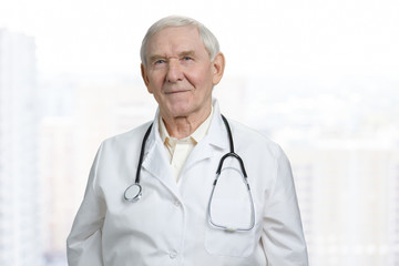 Fototapeta premium Portrait of smiling old caucasian doctor in lab coat. Senior physician in stethoscope in bright background.