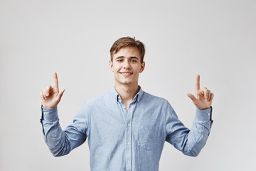Young handsome man is looking up, pointing his fingers hoping that all the numbers in his lottery...
