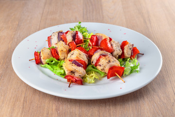 chicken fillet kebabs with roasted peppers, onions and lettuce on wooden skewers are on the plate