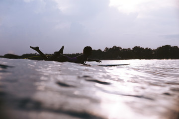 silhouette of sportswoman lying on surfing board in ocean on sunset