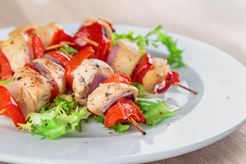 chicken fillet kebabs with roasted peppers, onions and lettuce on wooden skewers are on the plate
