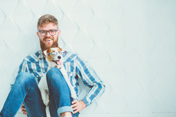Friendly hipster handsome beard guy in eyewear holding smart pet Jack russell terrier dog in eyeglasses on white polygonal background. Vision, health and protection concept.
