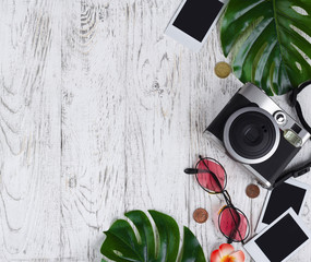 Flatlay with camera, blank photo, coins, sunglasses, leaves on the white desk.