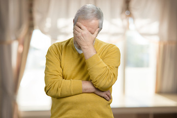 Portrait of old grandpa doing facepalm. Forgetful old man holding his hand to his forehead.