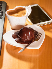 Cup of coffee and chocolate cake next to computer.