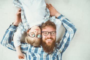 Top view portrait of happy beard father and son in eyeglasses lying on the white floor background....