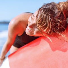 Fototapeta na wymiar beautiful young smiling girl lying on surfboard on beach