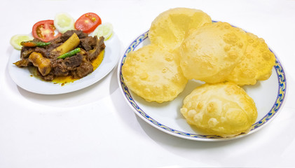 Traditional homemade Bengali Indian meal of deep fried poori made from wheat flour with spicy mutton curry garnished with vegetables.