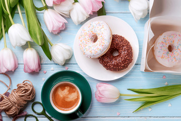 Fototapeta na wymiar donuts, coffee and tulips on a blue wooden background.