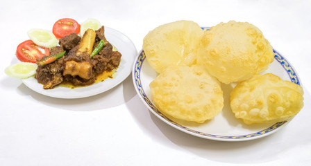 Traditional homemade Bengali Indian meal of deep fried poori made from wheat flour with spicy mutton curry garnished with vegetables.