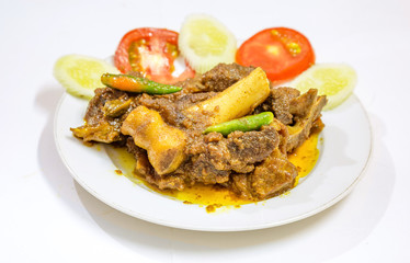 Popular Indian Bengali food meal of spicy mutton curry popularly known as mutton kosha with green chili and sliced tomato and cucumber.