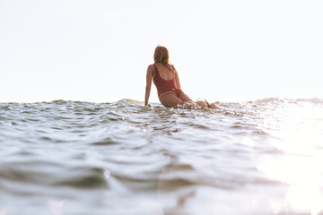 back view of woman in swimming suit surfing in ocean