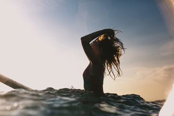 silhouette of woman readjusting hair while sitting on surfing board in ocean