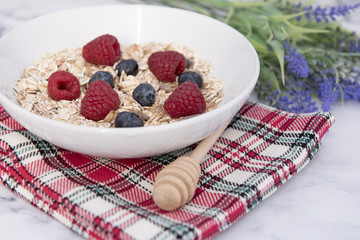 White bowl of muesli with raspberries, blueberries and lavender in the background 