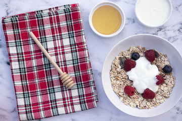 White bowl of muesli with raspberries, blueberries and a pot of honey and yogurt 