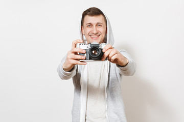 Young handsome excited man student in t-shirt and light sweatshirt with hood with headphones holds retro camera in hands and shows it to camera isolated on white background. Concept of photography