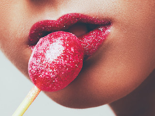Woman licking a red shiny lollipop candy. Close up against white background