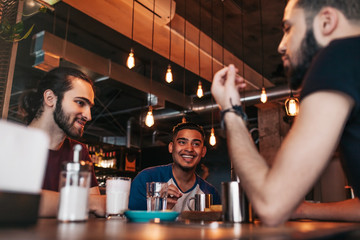 Happy arabian young men hanging in loft cafe. Best friends talking in lounge bar. Spending free...