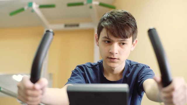 A 15 year old guy in the hearing aids trains in the gym. the young man trains on an exercise bike.