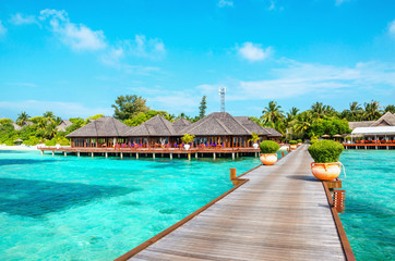 Fototapeta na wymiar Wooden pier and exotic bungalow on the background of a sandy beach with tall palm trees, Maldives