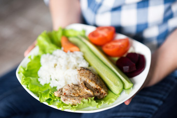 Girl with a plate of vegetables in hands. Healthy eating concept. A girl in jeans and a plaid shirt. Casual Style. Proper nutrition. Diet. Health. Chicken meat with spices. Small depth of field.