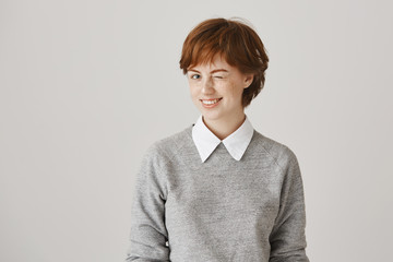 If you know what I mean. Studio shot of positive attractive redhead woman with freckles winking as if being on same line with friend, agreeing with idea, standing over gray background