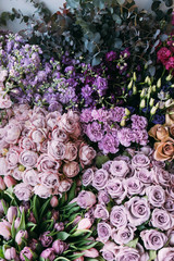 Beautiful freshly delivered blossoming flowers (roses, tulips,ranunculus,mattiola, eucalyptus) in pastel purple colors at the florist shop stacked together into a texture, top view, flat lay