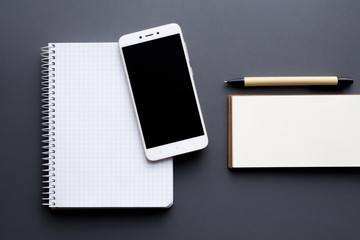 blank notepad and notebook with smartphone and pen over gray background