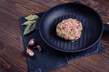 Cast-iron frying pan with a Patty made of minced meat with herbs on the stone and wooden background