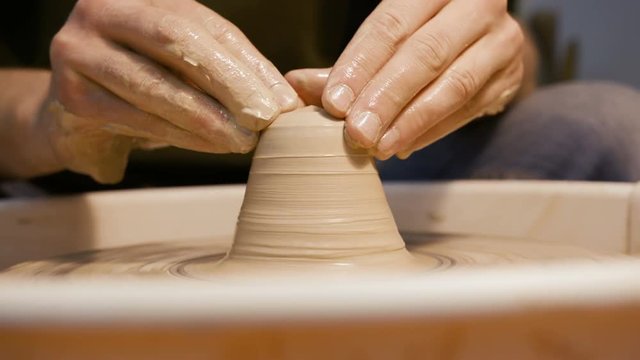 Male craftsperson sculpt process on the round potterswheel closeup isolated. Artisan dexterity creating product - cup or vase from wet brown mud. Lifestyle, leisure, creativity concept of background