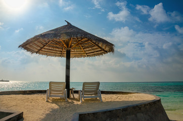 Sunbeds and palm tree umbrellas on a background of blue sky and azure water, Maldives