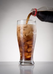 Pour cola from bottle to glass with ice on the gray background