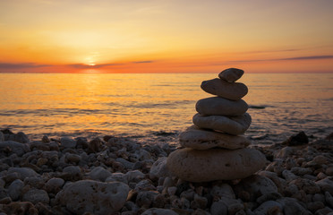 Pyramid of the small pebbles on the beach. Stones, against the background of the sea shore during sunset