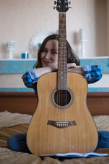 Smiling young woman with acoustic guitar in bedroom