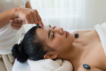 Fototapeta na wymiar Hand of woman masseur place the stone on the face of a girl asian in the spa salon. Beauty treatment and relaxing concept. Spa Hot Stones