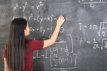 Beautiful young girl teacher writing physics formulas on blackboard.