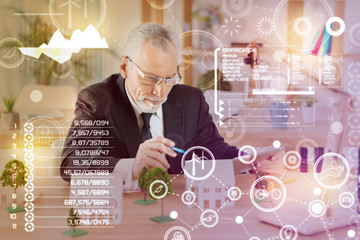 Comparing models. Clever concentrated smiling architect pointing to a miniature house while being at work