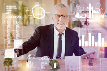 Cheerful specialist. Smart qualified professional architect feeling happy while sitting at the table and working with miniature houses