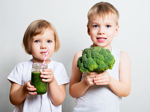 Two Pretty Fun Kids With Green Smoothies And Broccoli. Helthy And Clean Food For Children