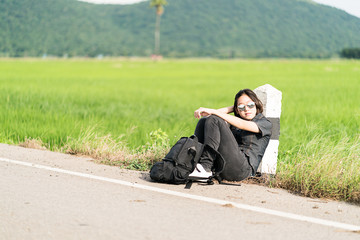 Naklejka na ściany i meble Woman sit with backpack hitchhiking along a road