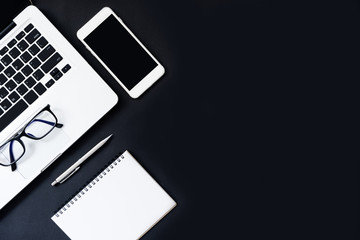 Black office desk table with laptop, smartphone and supplies. Top view, flat lay.